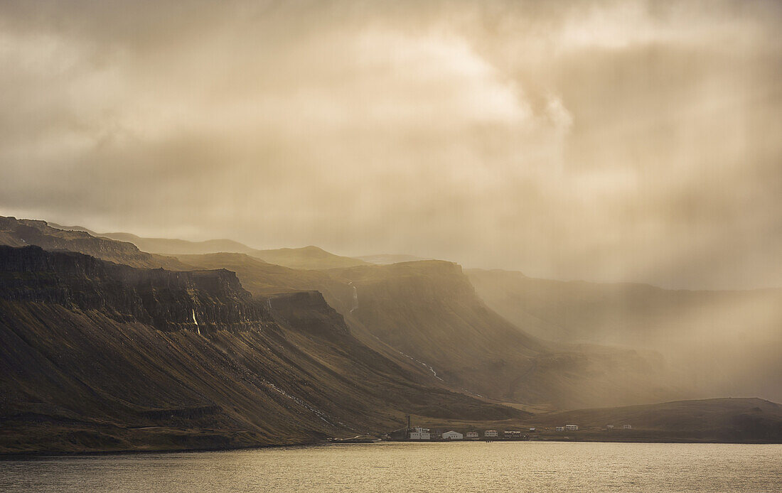 Lichtstrahlen leuchten auf die Berge und das verlassene Dorf Djupavik; Island
