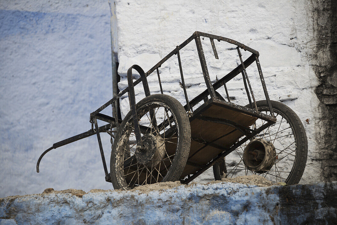 Old Cart Resting Amongst Faded Blue And White Painted Buildings; Chefchaouen, Morocco