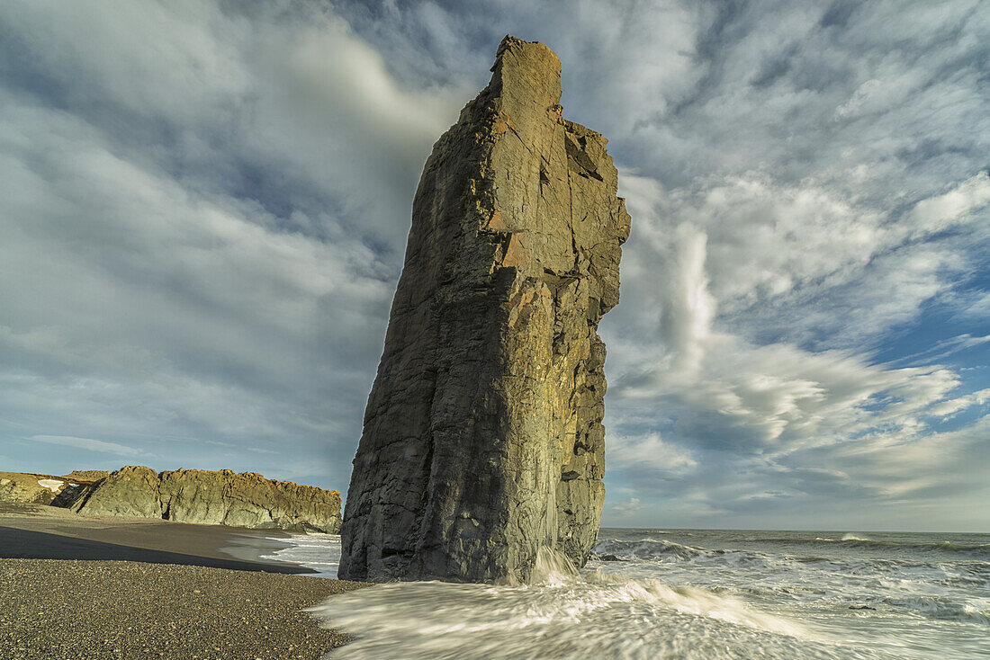 Ein Seestapel ragt aus dem Felsgestein, während die Wellen an den Stränden der Ostfjorde dagegen prallen; Island