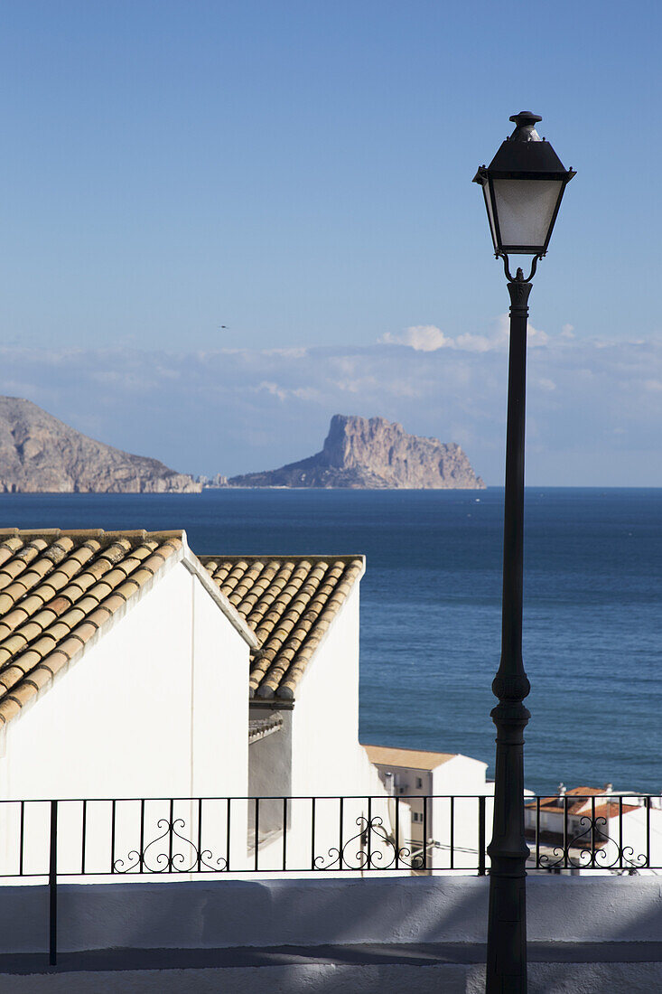 Laternenpfahl und Gebäude entlang der Küste mit einer zerklüfteten Küstenlinie in der Ferne; Altea, Spanien