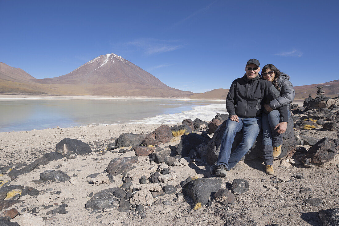 Couple Sitting On The Shores Of Laguna Verde, A Salt Lake On The Chilean Border; Bolivia