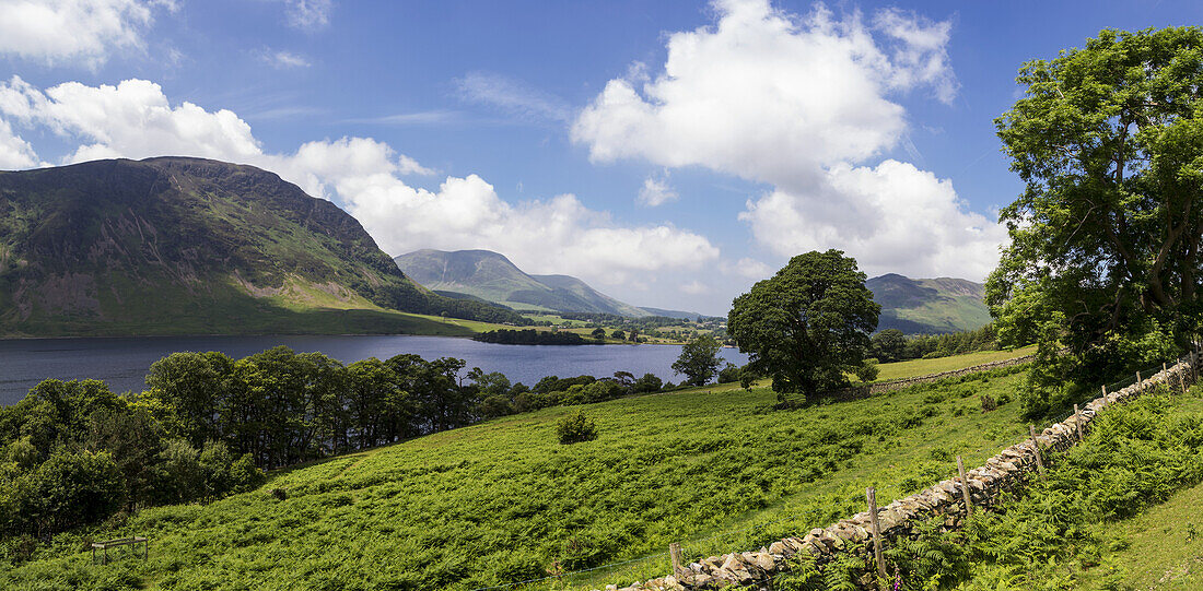 Ein ruhiger See zwischen Bergen und einer Steinmauer im Vordergrund; Cumbria, England