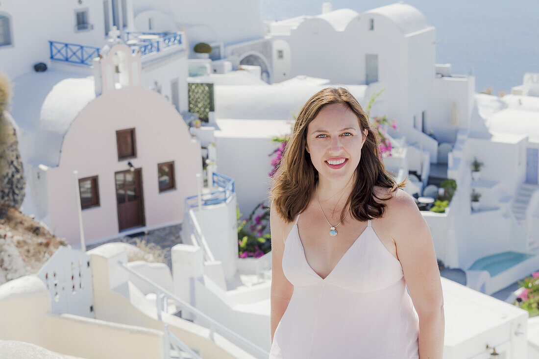 Eine Frau posiert mit einer weiß getünchten Kirche und Gebäuden im Hintergrund; Santorin, Griechenland
