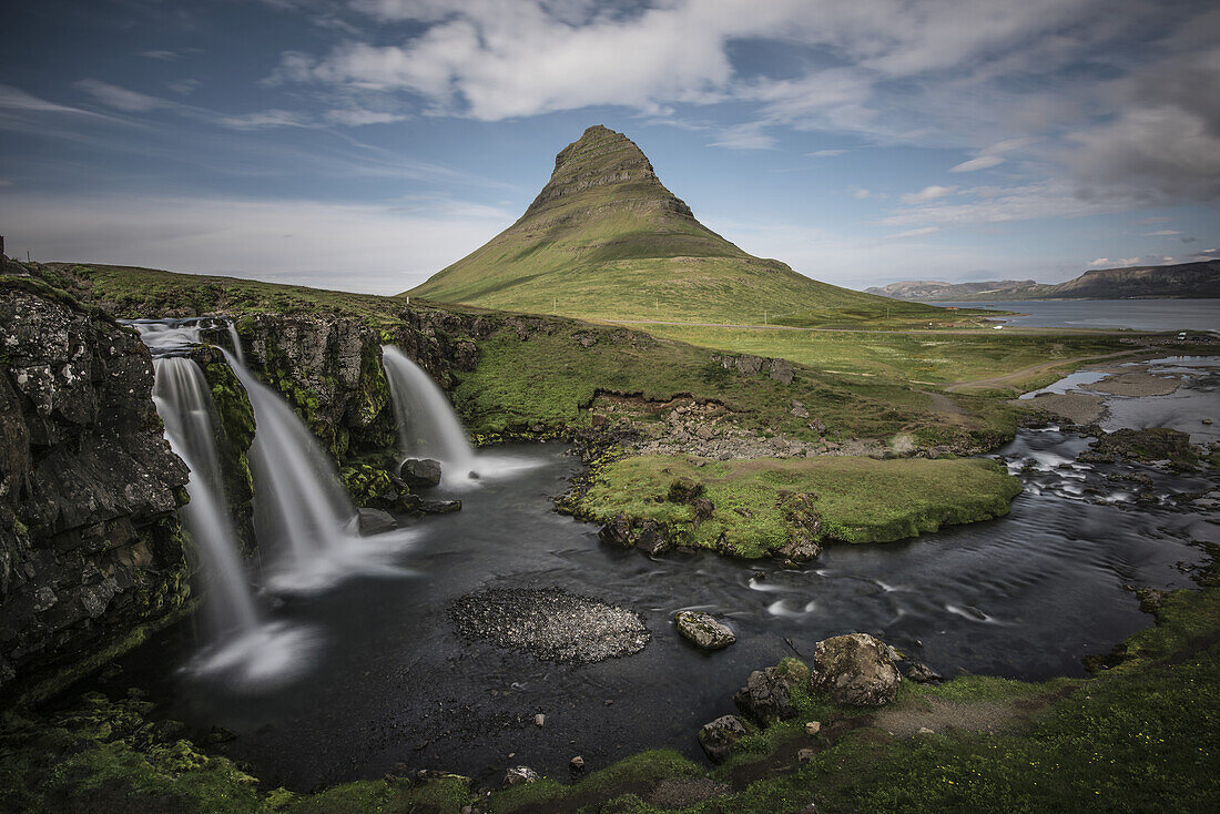 Wasserfälle und ein schroffer grüner Berggipfel in einer isländischen Landschaft; Island