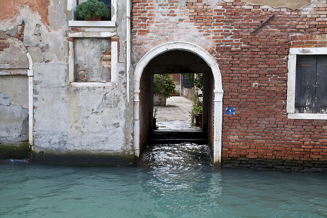 Gewölbte Türöffnung in einer Backsteinmauer an einem Kanal; Venedig, Italien