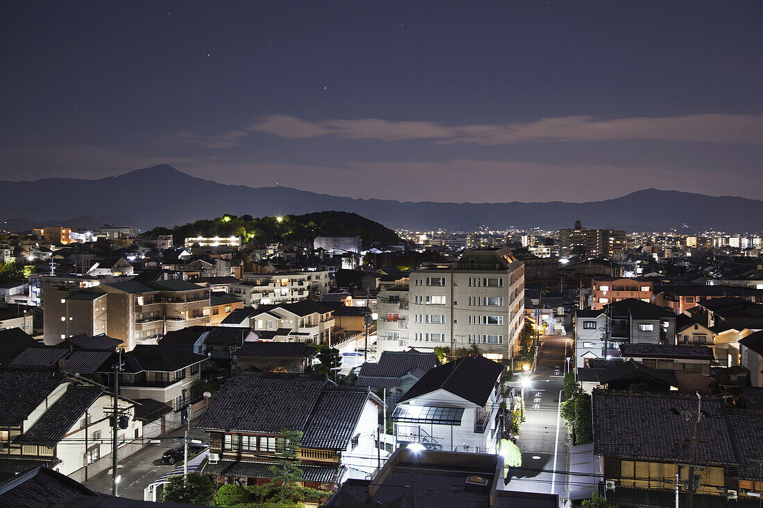 Beleuchtete Straßen und Gebäude in der Abenddämmerung, in der Ferne die Silhouette der Berge; Kyoto, Japan