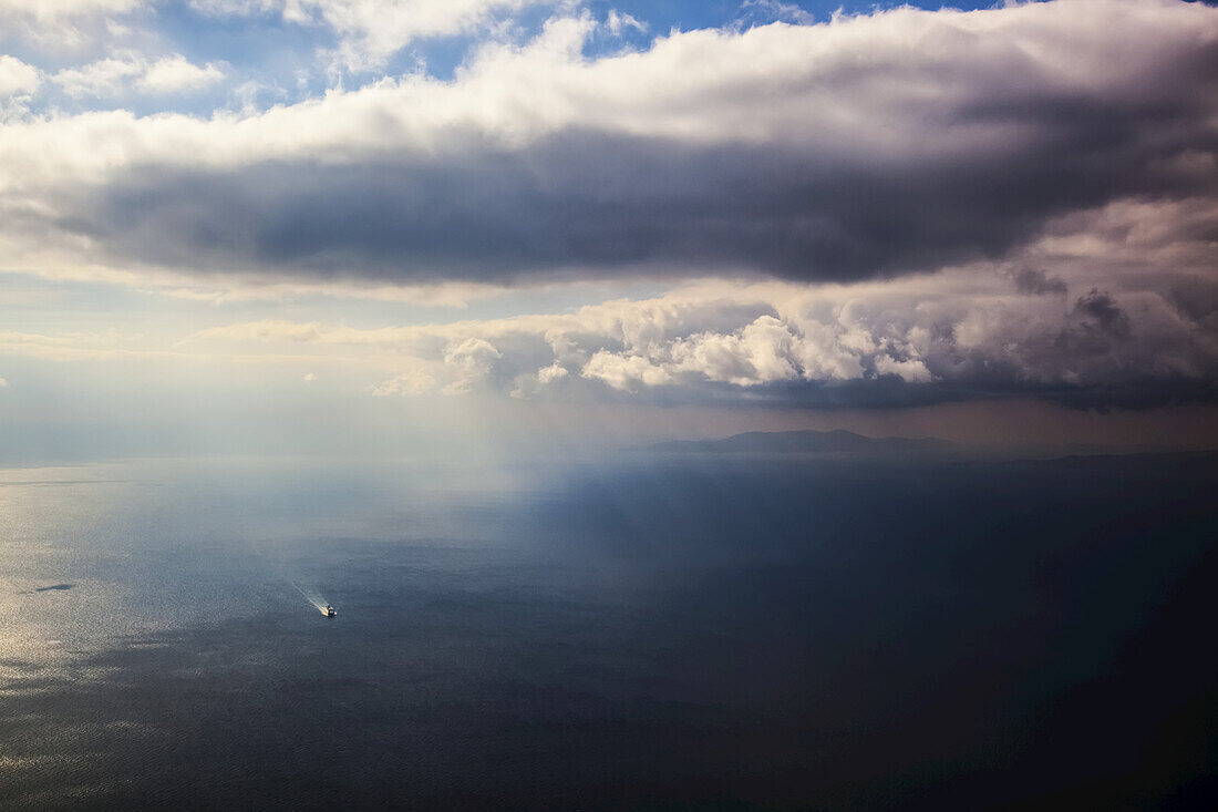 Ein einsames Boot auf dem Ägäischen Meer bei bewölktem Himmel und Fernsicht auf die Küste; Griechenland