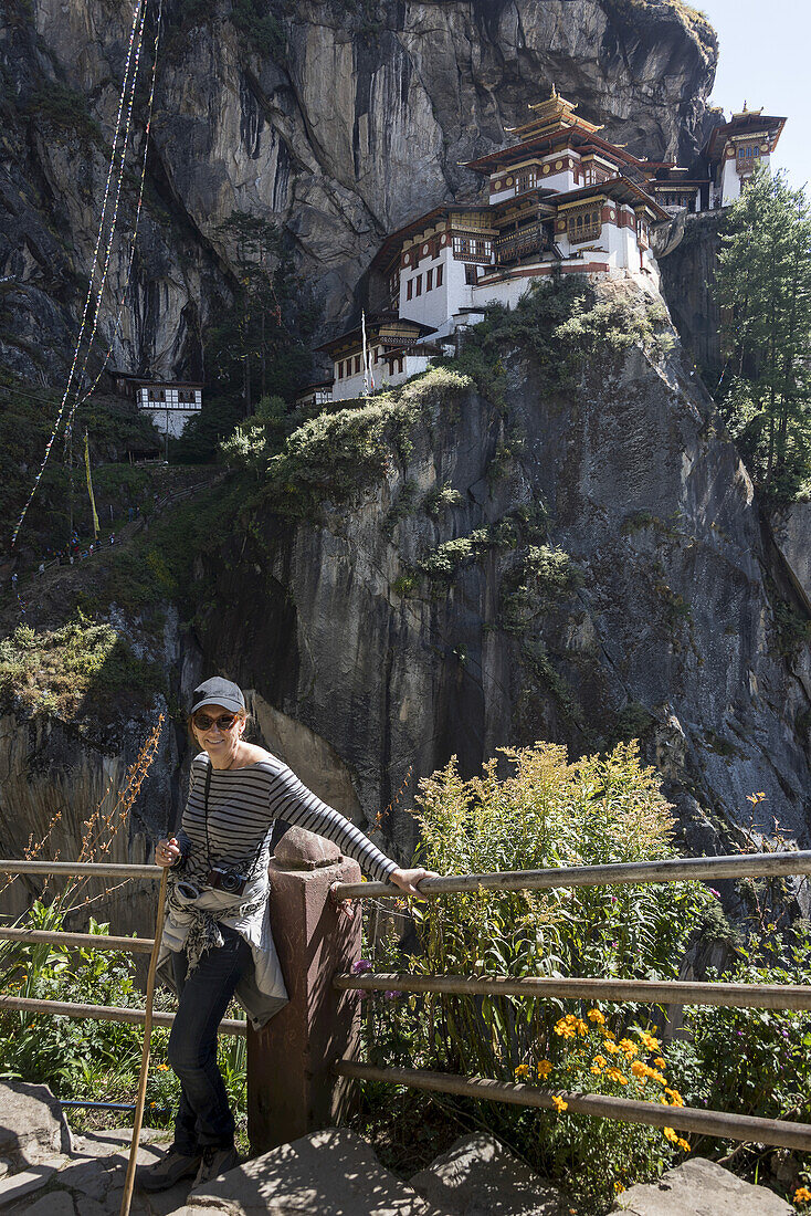 Eine Frau steht an einem Geländer mit dem Taktsang-Palphug-Kloster im Hintergrund; Paro, Bhutan