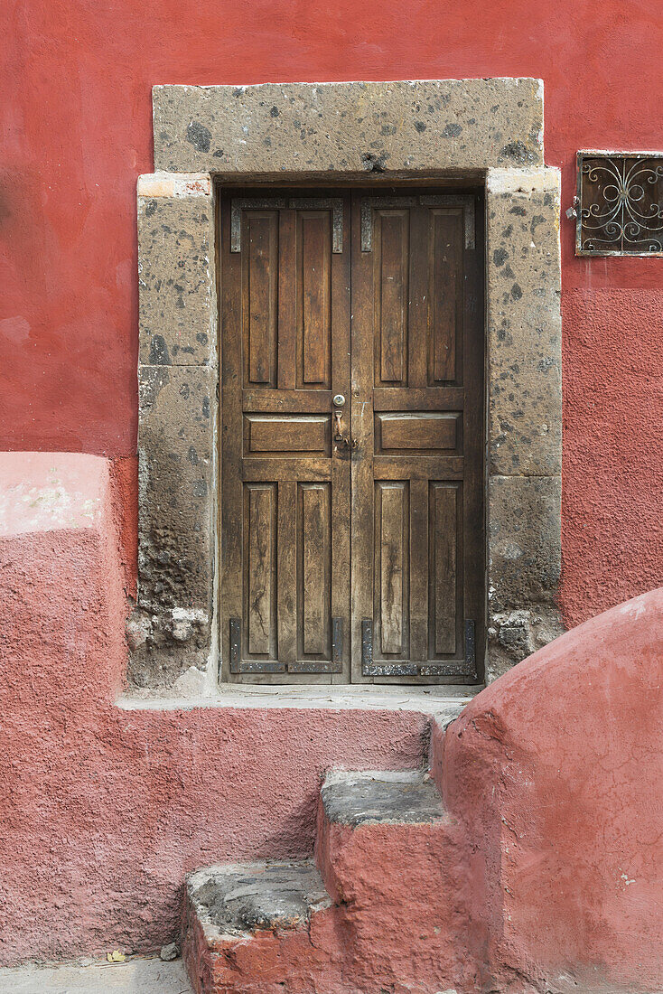 Abgenutzte Holztüren an einem rot gestrichenen Gebäude; San Miguel De Allende, Guanajuato, Mexiko