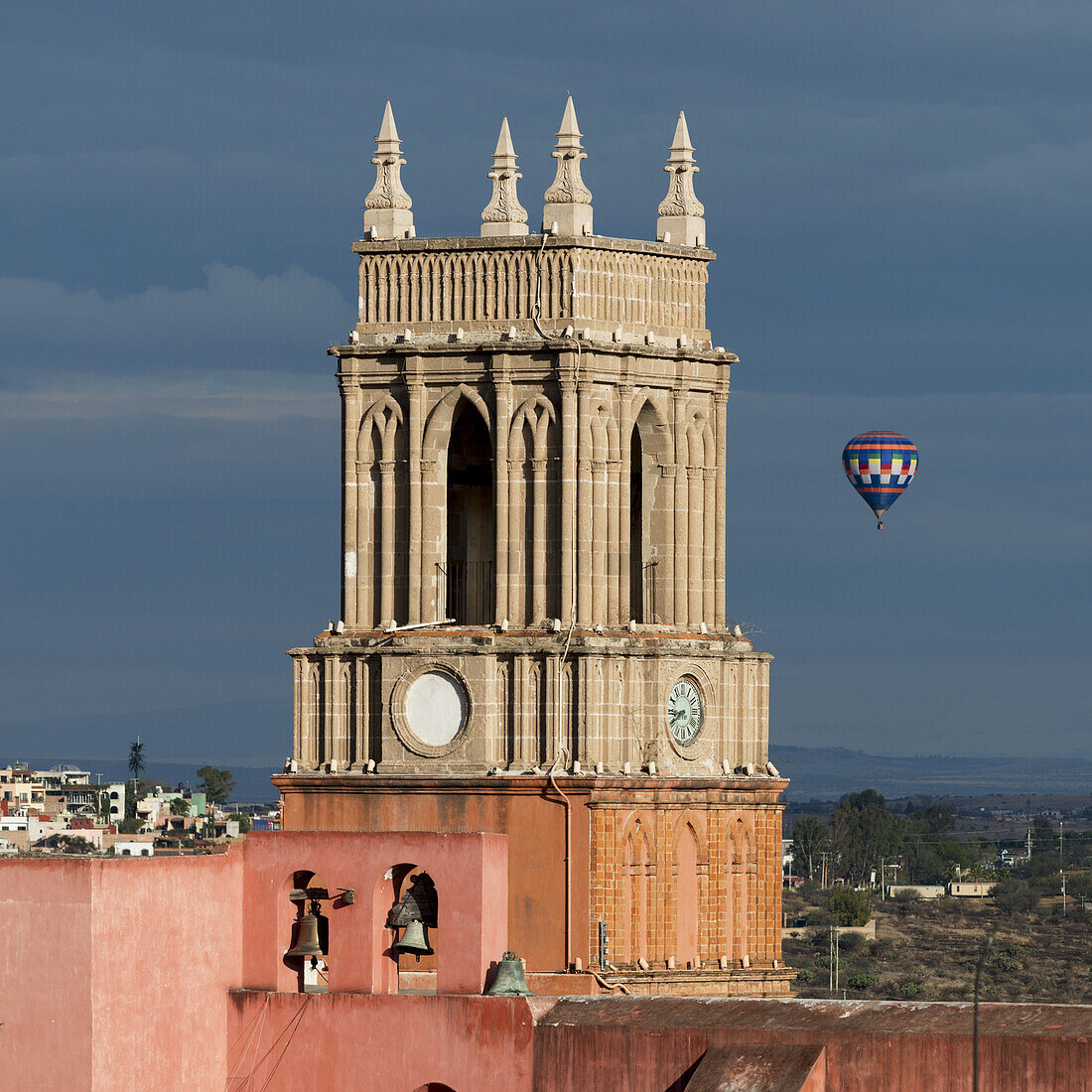 Clock Tower And Bells Of The Parish Church With A Hot Air Balloon Flight In The Distance; San Miguel De Allende, Guanajuato, Mexico