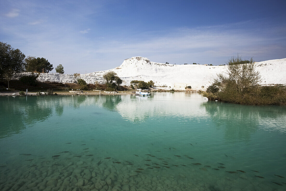 Türkisfarbenes Wasser in einem Pool, in dem sich eine weiße Wand aus Mineralablagerungen spiegelt; Pamukkale, Türkei