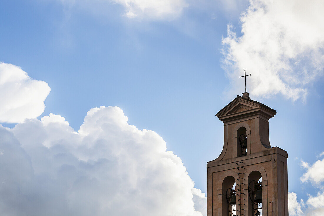 Kreuz und Glockenturm einer Kirche vor einem blauen Himmel mit Wolken; Rom, Italien