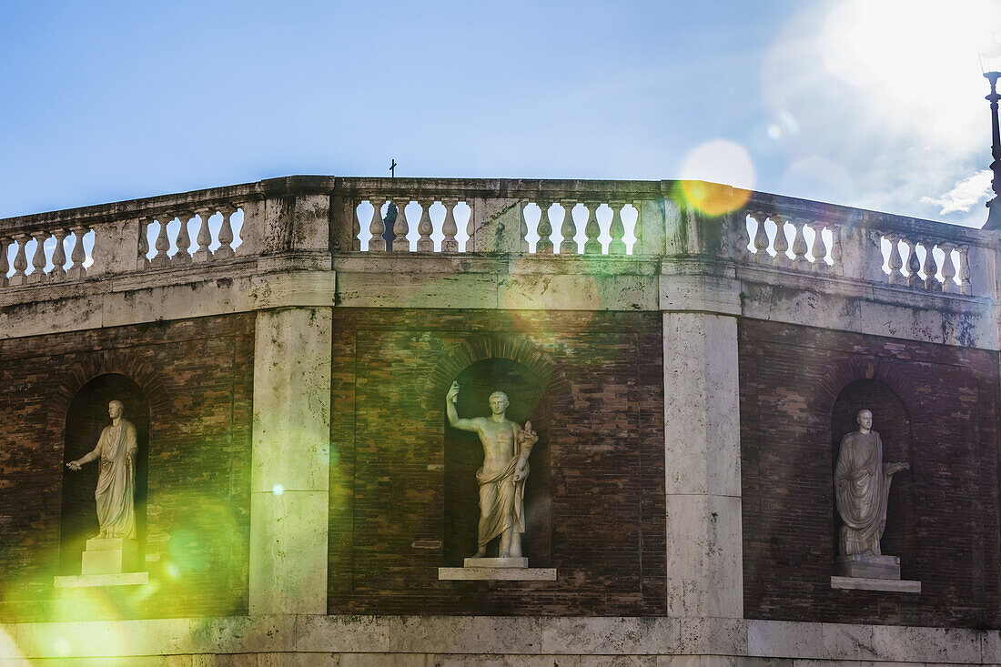 Statuen in Nischen an einer Backsteinmauer mit Balustraden entlang der Oberseite, auf die das Sonnenlicht fällt, Piazza Del Quirinale; Rom, Italien