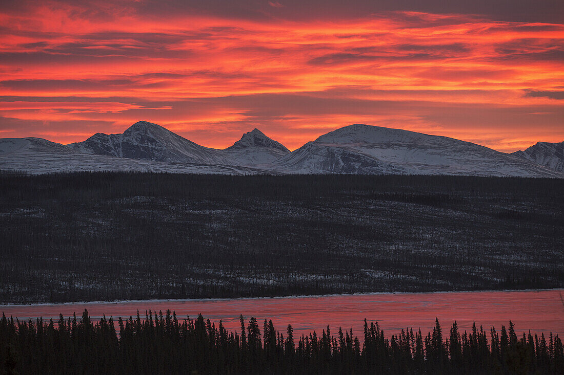 Sonnenuntergang über der Rancheria-Bergkette und dem eisbedeckten Swan Lake; Yukon, Kanada
