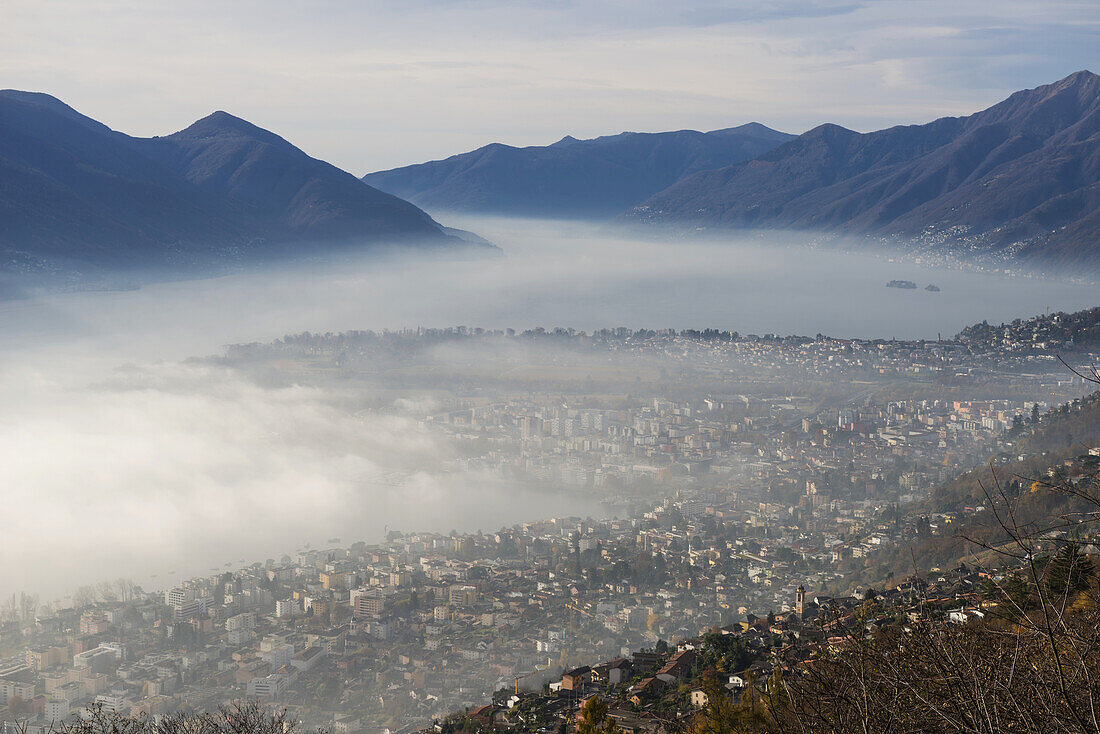 Nebel setzt über einer Stadt und einem Alpensee ein; Locarno, Tessin, Schweiz