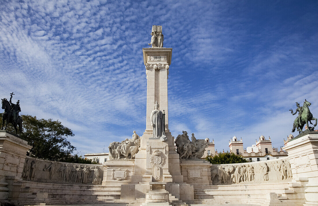 In eine Wand geschnitzte menschliche Figuren und ein Turm mit einer Statue vor einem blauen Himmel mit Zirruswolken; Andalusien, Spanien