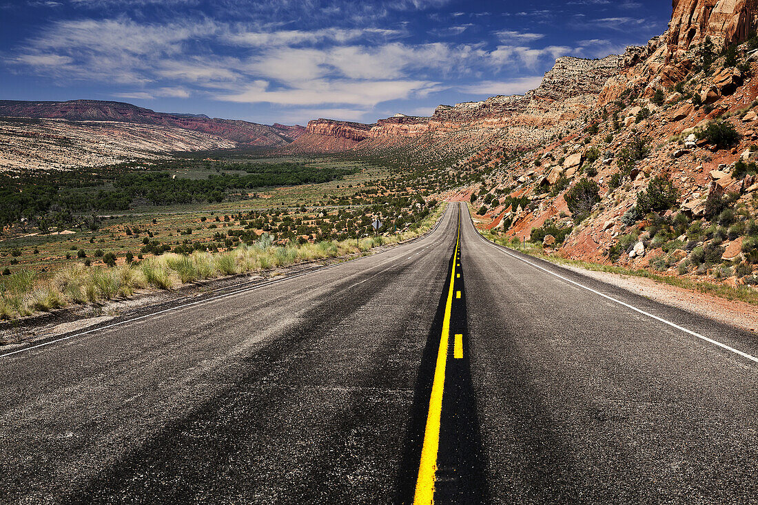 Utah Highway Stretching Into The Distance With Rock Cliffs Wrapping From The Right Side Foreground Around To The Background Center And Left Of The Photo With Blue Skies With Some Clouds; Utah, United States Of America