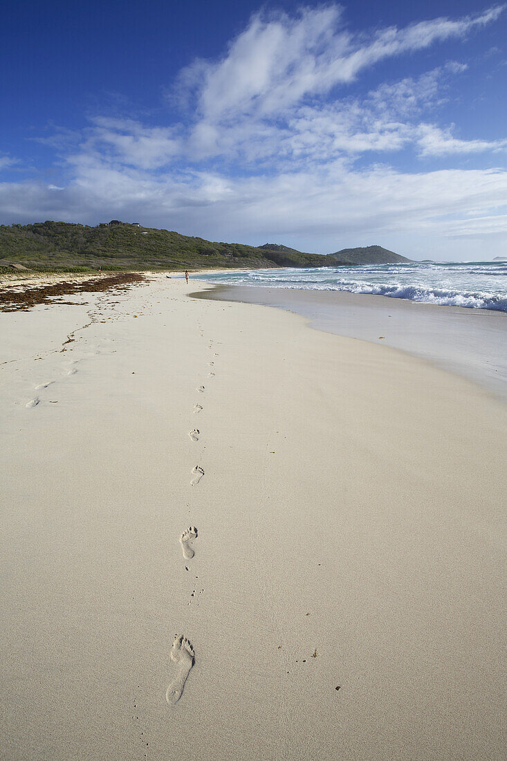 Fußabdrücke im weißen Sandstrand mit Meeresbrandung
