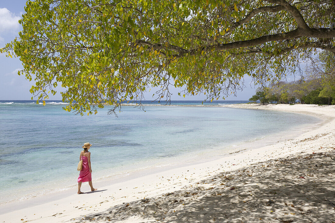 Frau im Bikini spazierend am Ufer eines weißen Sandstrandes