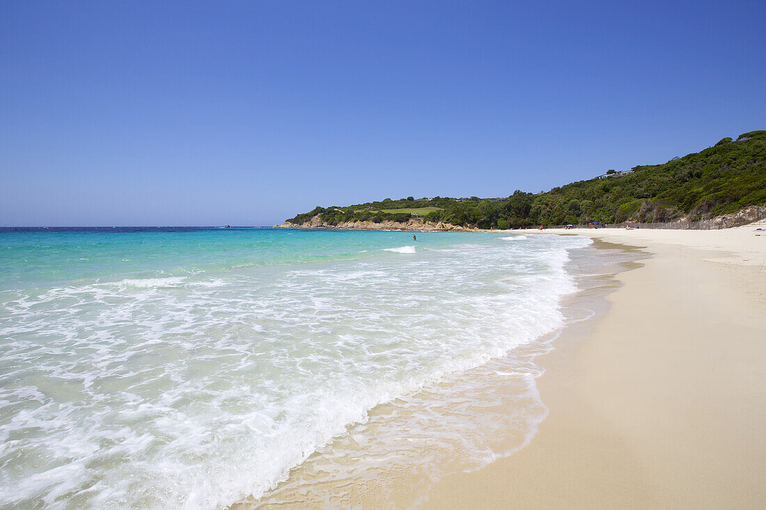 Weißer Sandstrand mit blauem Meer und Himmel und grüner Landzunge