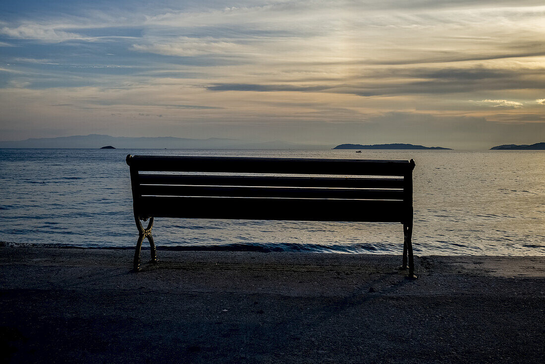 Silhouette Of A Bench At The Water's Edge On A Beach At Sunset Along The Aegean Sea; Panormos, Thessalia Sterea Ellada, Greece