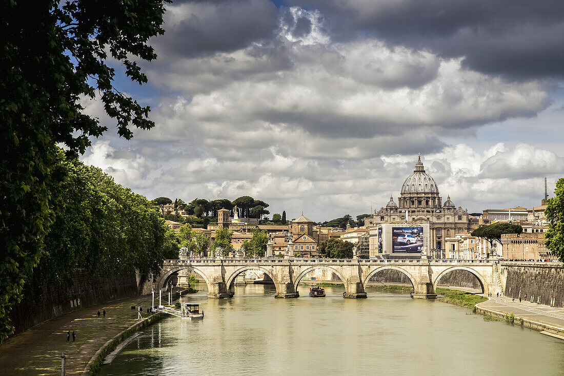 Blick auf den Petersdom in der Ferne mit einer Brücke und moderner Autowerbung über den Tiber; Rom, Italien