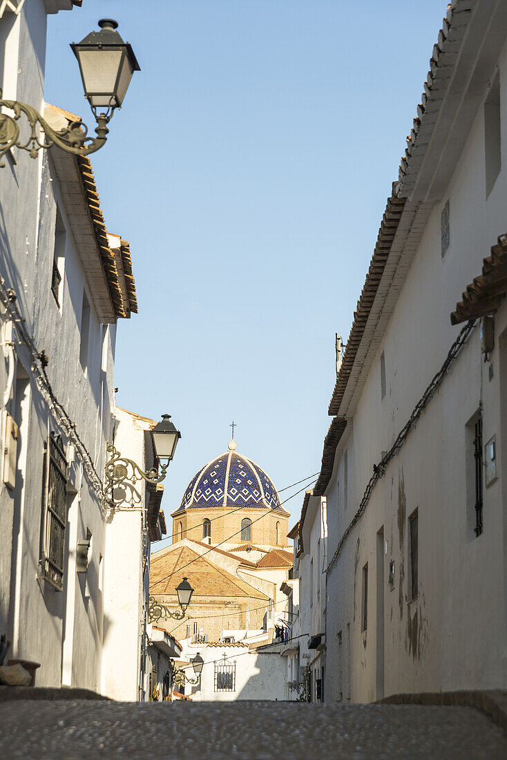 Straße im Stadtzentrum von Altea, einer schönen Stadt an der Costa Blanca, mit der Kuppel der Kirche im Hintergrund; Altea, Alicante, Spanien