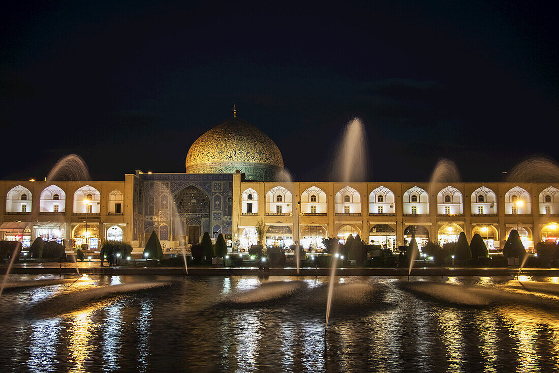 Lichter, die Wasserfontänen und ein Gebäude bei Nacht beleuchten; Isfahan, Iran