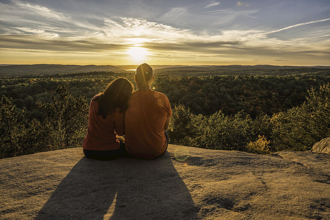 Paar sitzt auf einer Klippe mit Blick auf den Algonquin Park bei Sonnenuntergang; Ontario, Kanada