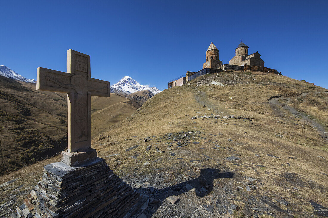 Steinkreuz und Dreifaltigkeitskirche von Gergeti mit dem Berg Kazbek im Hintergrund; Kazbegi, Mzcheta-Mtianeti, Georgien