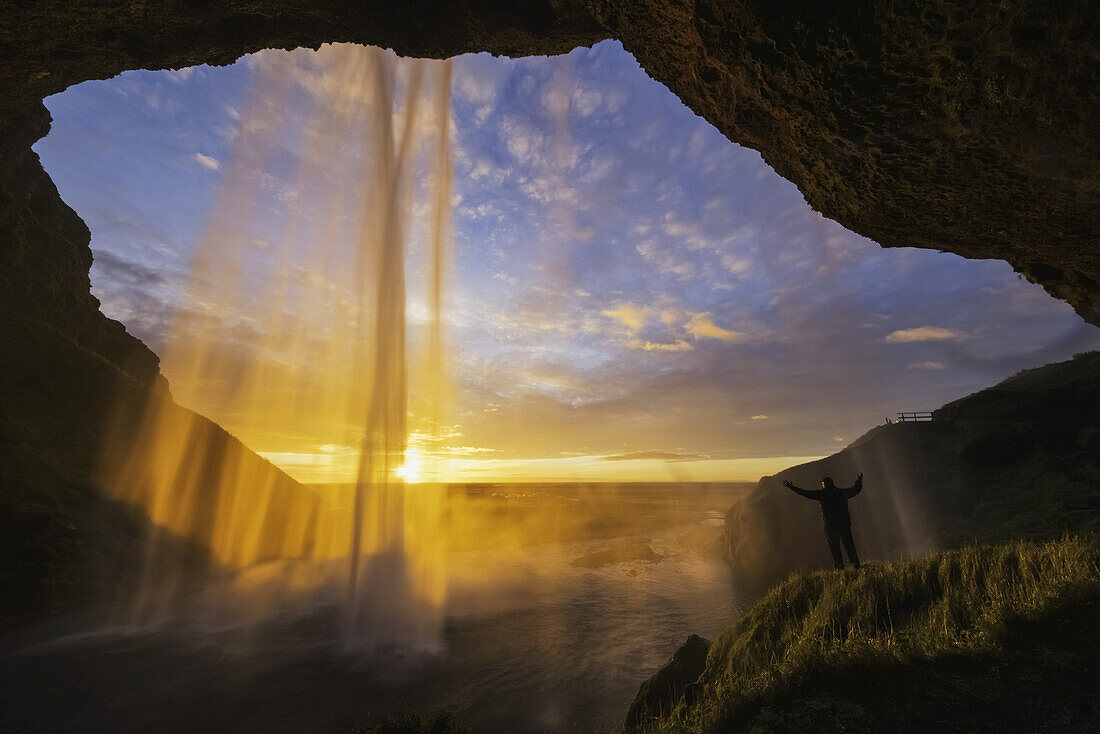 Mann steht hinter dem Wasserfall Seljandafoss an der Südküste Islands; Island