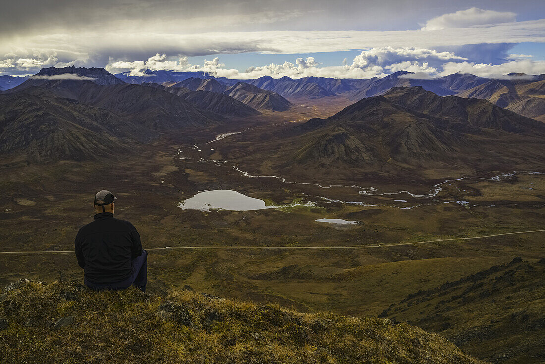 Man Stitting On A Look Out Overlooking The Blackstone Valley, Along The Dempster Highway; Yukon, Canada