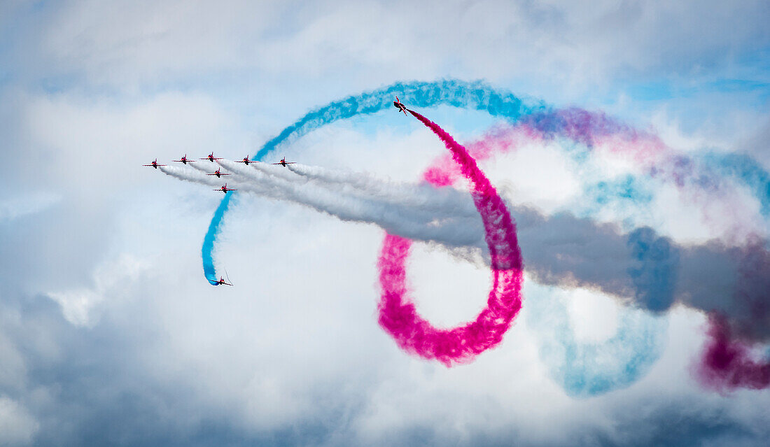 Red Arrows Flugschau, neun Flugzeuge fliegen in Formation mit bunten Kondensstreifen; South Shields, Tyne and Wear, England