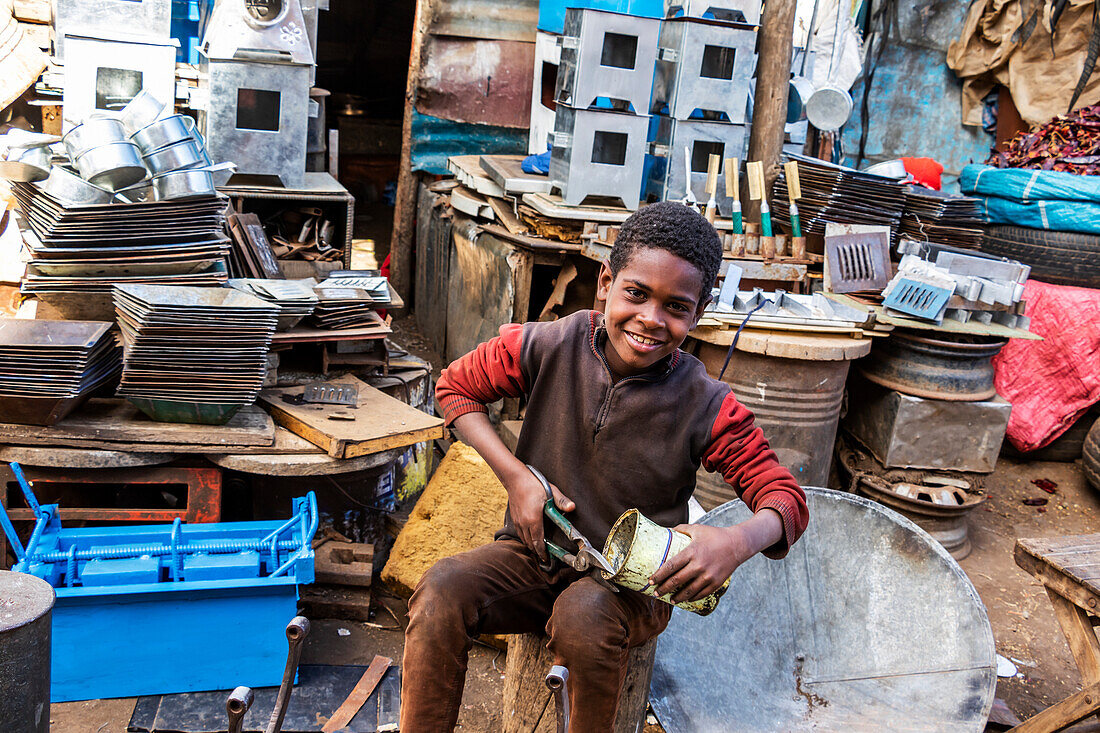 Eritreischer Junge beim Schneiden einer Dose auf dem Medeber-Markt, wo Kunsthandwerker alte Reifen und Dosen zu neuen Kunstgegenständen verarbeiten; Asmara, Zentralregion, Eritrea