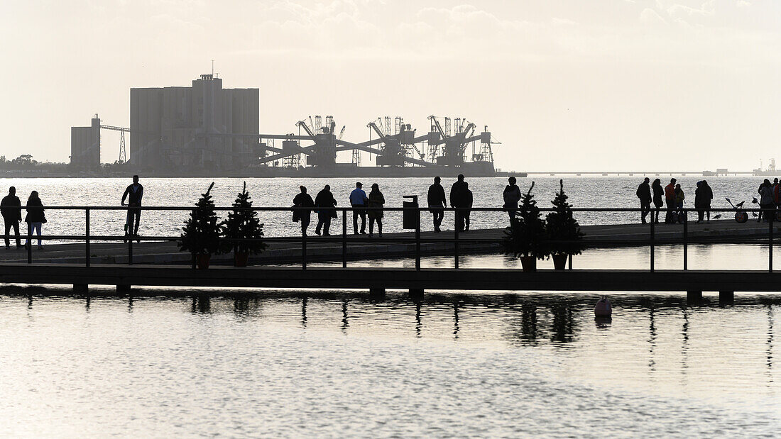 Silhouetted pedestrians on a pier on the Tagus River at dusk; Lisbon, Setubal District, Portugal