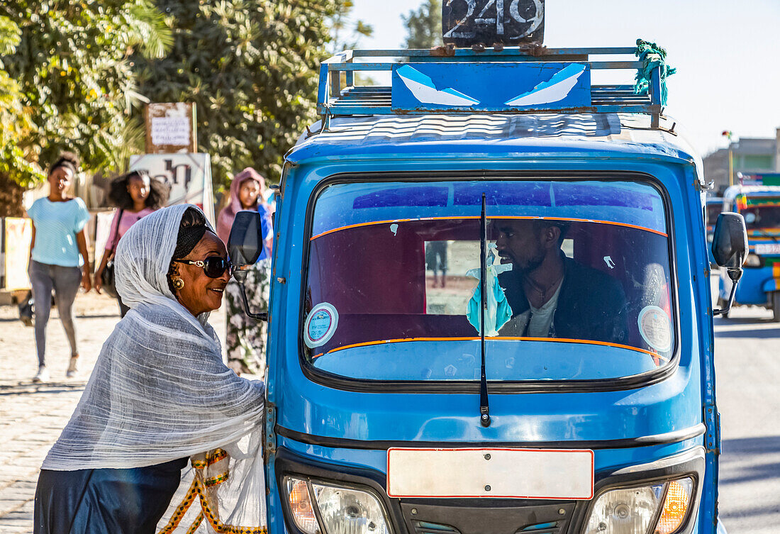 Frau an einer Auto-Rikscha, die sich durch das Fenster mit dem Fahrer unterhält; Wukro, Region Tigray, Äthiopien