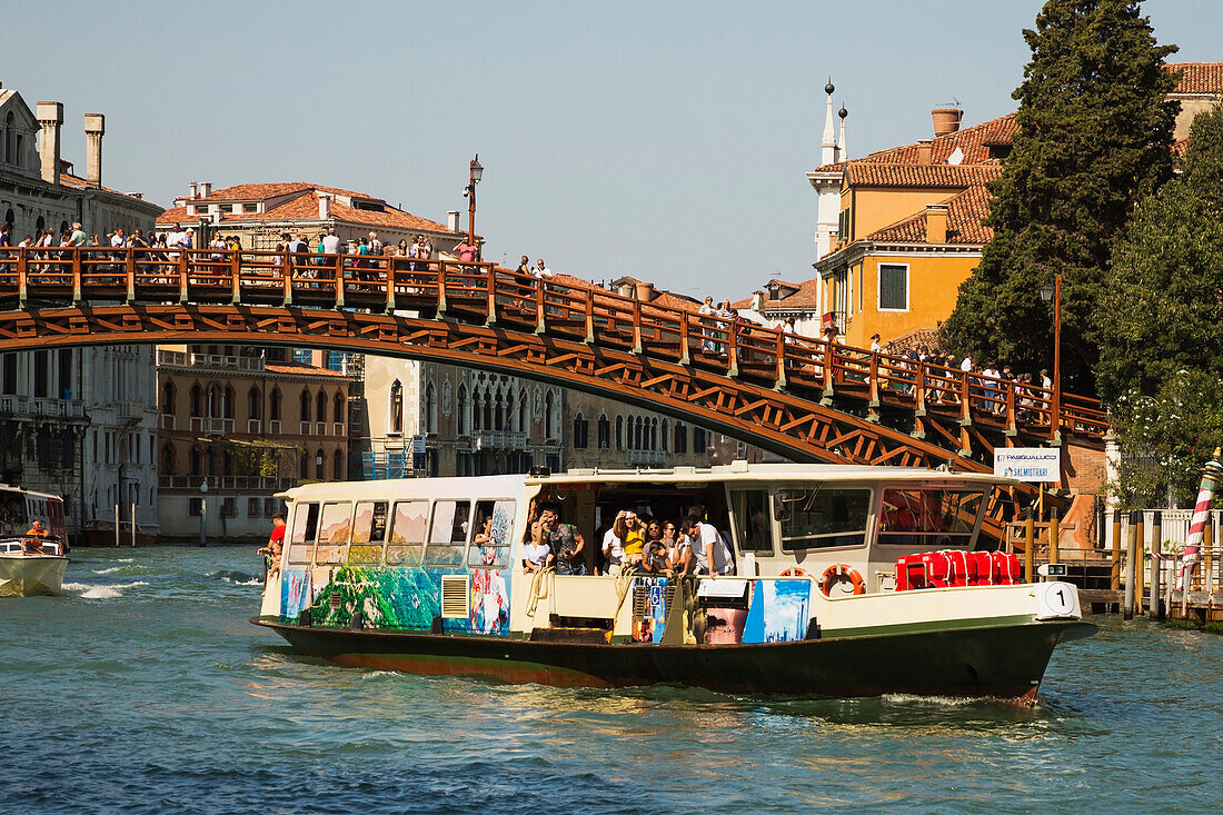 Accademia footbridge with tourists over Grand canal with vaporetto, water taxi and Renaissance architectural style residential palace buildings, San Marco; Venice, Veneto, Italy