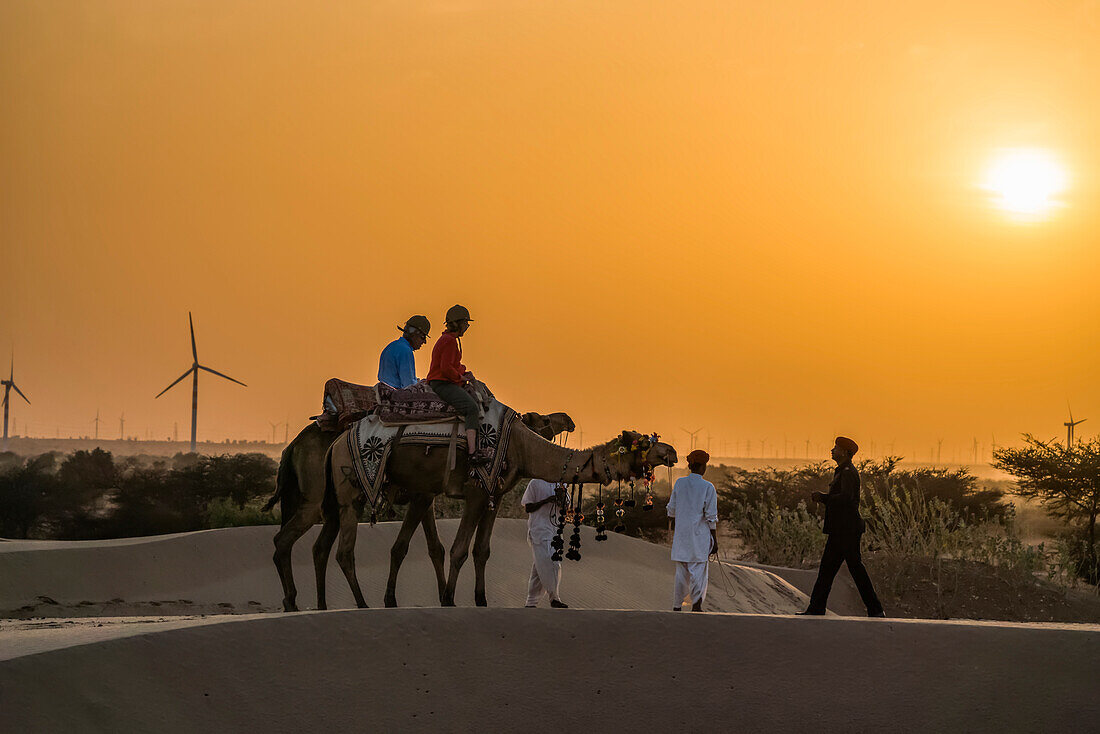 Menschen reiten mit Kamelen in der Wüste bei Sonnenuntergang; Rajasthan, Indien