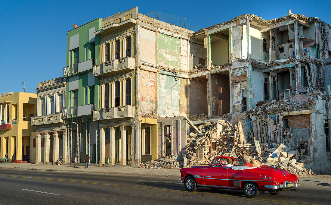 An old car passes the demolished facade of old buildings along a street; Havana, Cuba