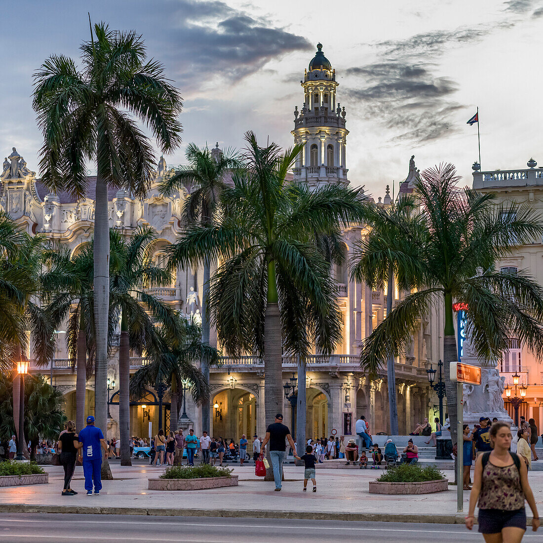 Pedestrians in a town square at dusk with palm trees and a tower in the distance; Havana, Cuba