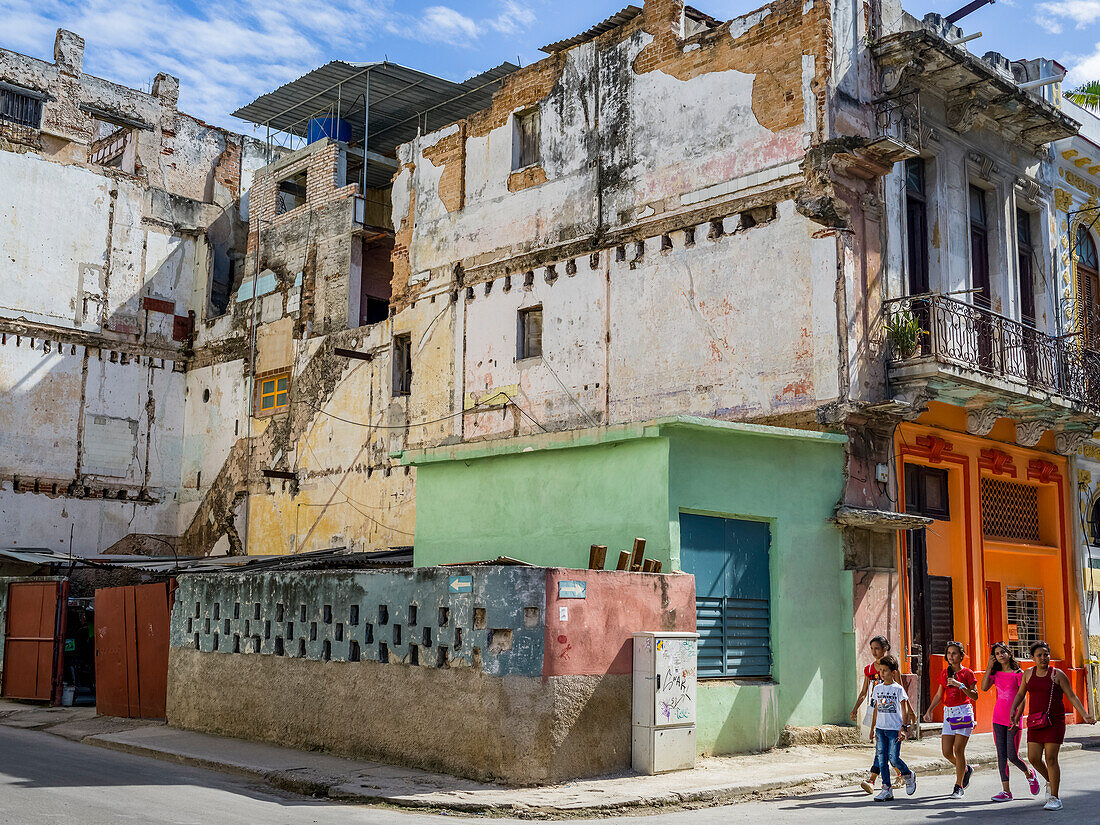 Pedestrians walk on the street past a run-down building; Havana, Cuba