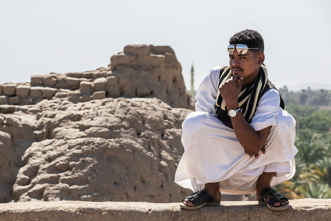 Junger sudanesischer Mann, der selbstbewusst an einer Felswand hockt; Kerma, Nordstaat, Sudan