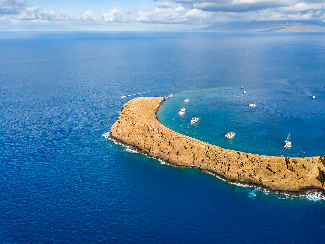Molokini Crater, aerial shot looking at the backwall of the crescent shaped islet at mid-morning with charter boats inside; Maui, Hawaii, United States of America