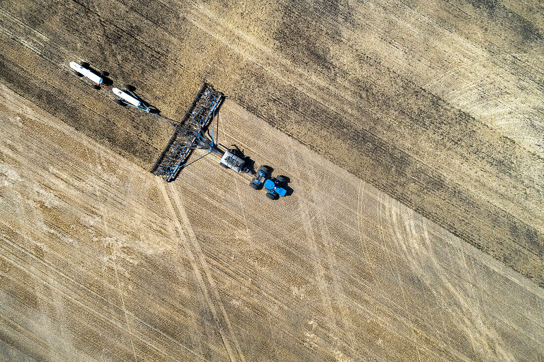 Aerial view of air seeder in field with white ammonia tanks, near Beiseker; Alberta, Canada