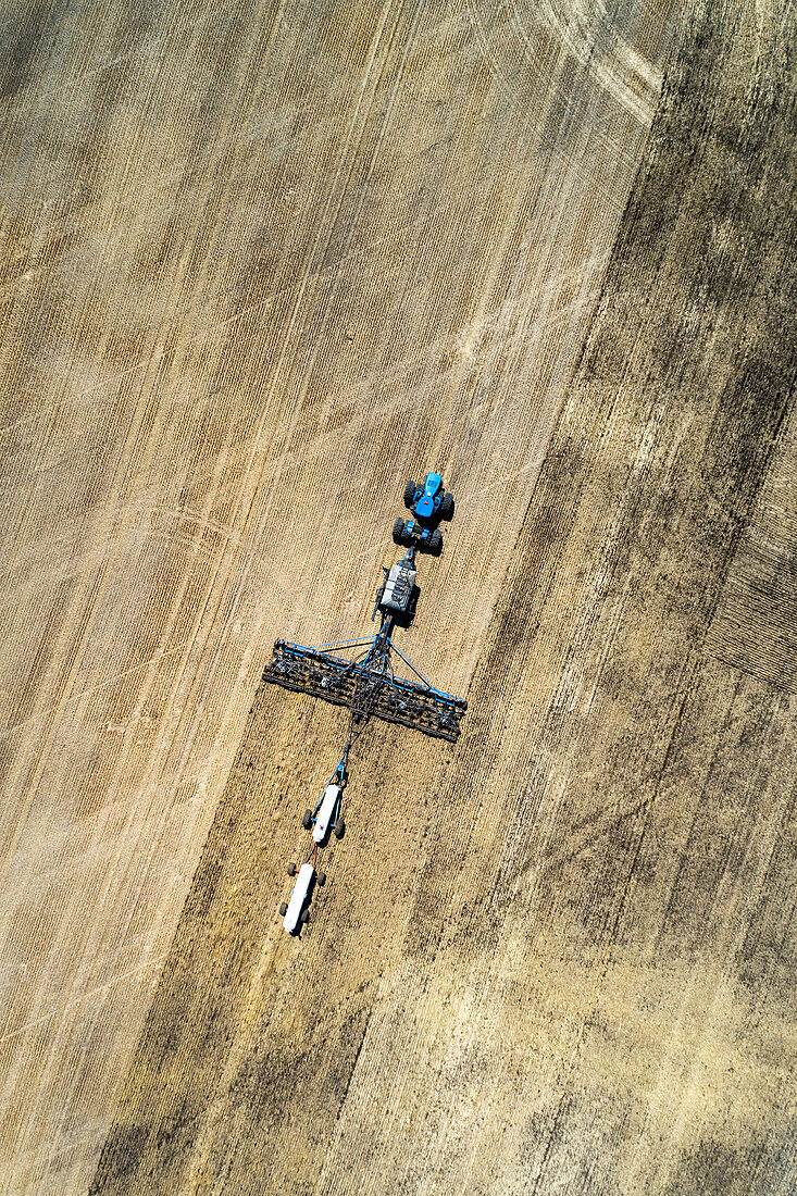 Luftaufnahme einer Einzelkornsämaschine auf einem Feld mit weißen Ammoniaktanks in der Nähe von Beiseker; Alberta, Kanada