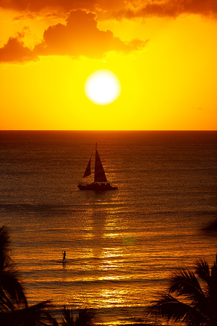 Golden sunset off Waikiki Beach with a silhouetted sailboat in the water; Honolulu, Oahu, Hawaii, United States of America