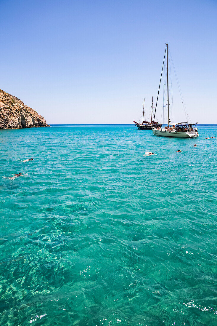Touristen schwimmen im klaren, türkisfarbenen Wasser der Bucht von Galazia Nera, in der Segelboote vor Anker liegen; Insel Polyaigos, Kykladen, Griechenland