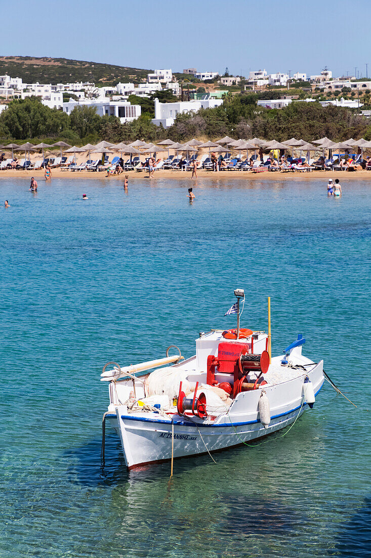 Im Wasser vertäutes Fischerboot mit Schwimmern und Sonnenanbetern in der Santa Maria Beach Area; Paros Insel, Kykladen, Griechenland