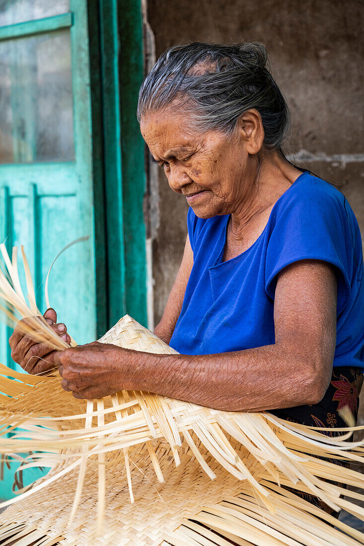 Eine ältere Frau flechtet einen Korb; Sidetapa, Bali, Indonesien