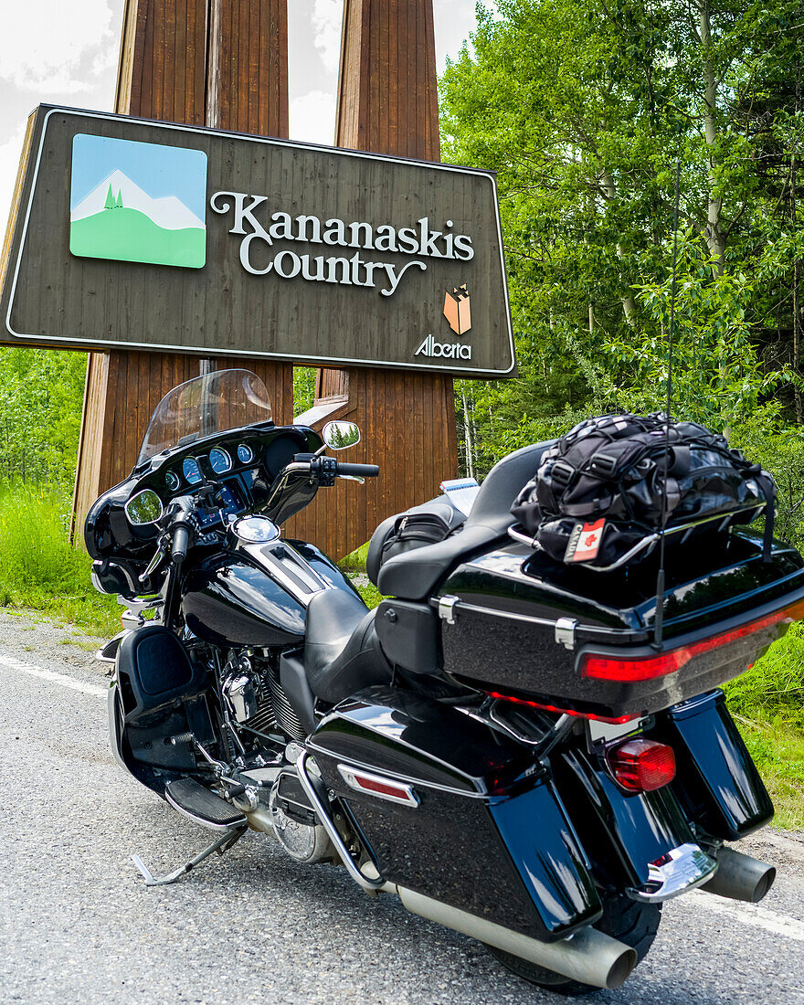 A motorcycle parked on the roadside of Bighorn Highway (Highway 40) in front of a sign for Kananaskis Country, Peter Lougheed Provincial Park; Alberta, Canada